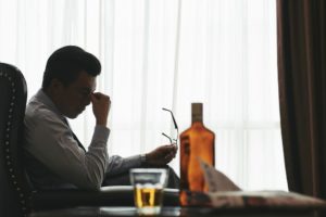 man looking stressed at desk with bottle of alcohol