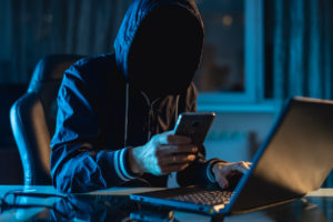 Anonymous hacker holding phone on computer