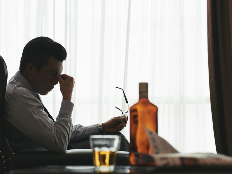 man looking stressed at desk with bottle of alcohol